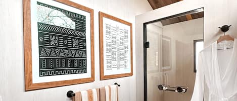A bathroom with wooden flooring, a mirror, a towel rack with towels, and two framed pictures on the wall.