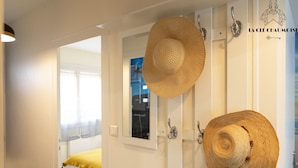 A room with a bed, a mirror, and two hats hanging on the wall.
