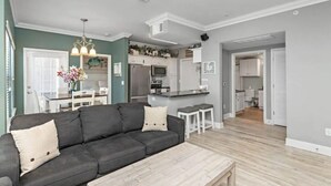Ein modernes Wohnzimmer mit einem dunkelgrauen Sofa, einem Holztisch und einem Essbereich mit weißem Tisch und Stühlen.