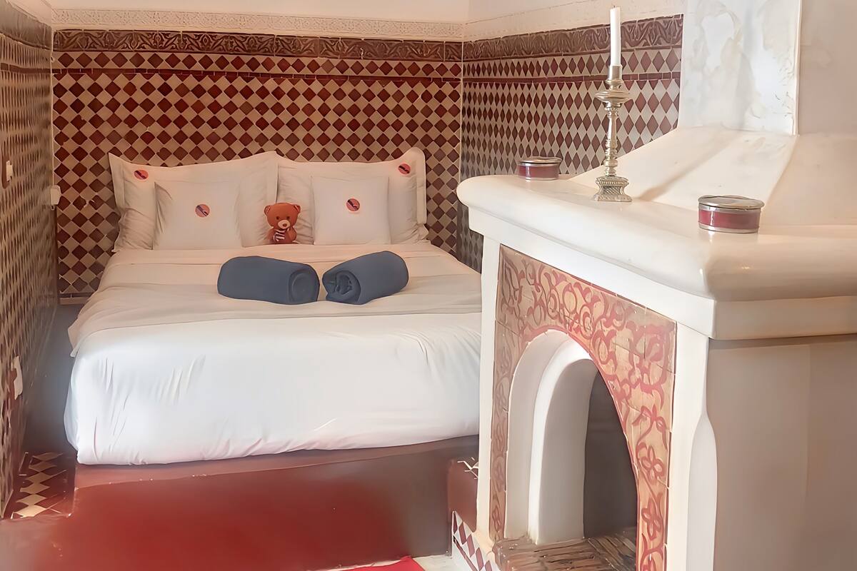 A hotel room with a bed, a painting, a decorative wall, a fireplace, and a red rug.