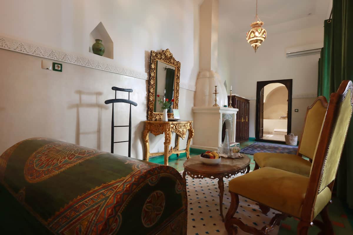 A traditional room with a patterned sofa, a wooden chair, a mirror, and a small table with a decorative item.