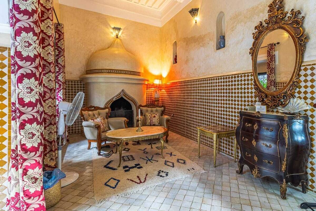 A traditional Moroccan interior with a tiled floor, ornate furniture, a fireplace, and a decorative mirror.