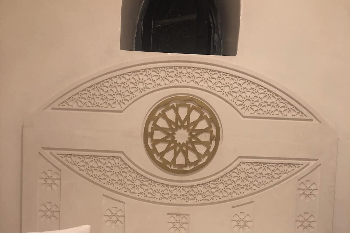 A bed with a decorative headboard featuring a central circular design and symmetrical patterns.