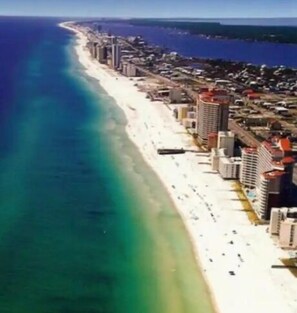 Una vista aerea di una città costiera con una lunga spiaggia, edifici alti e un mare blu limpido.
