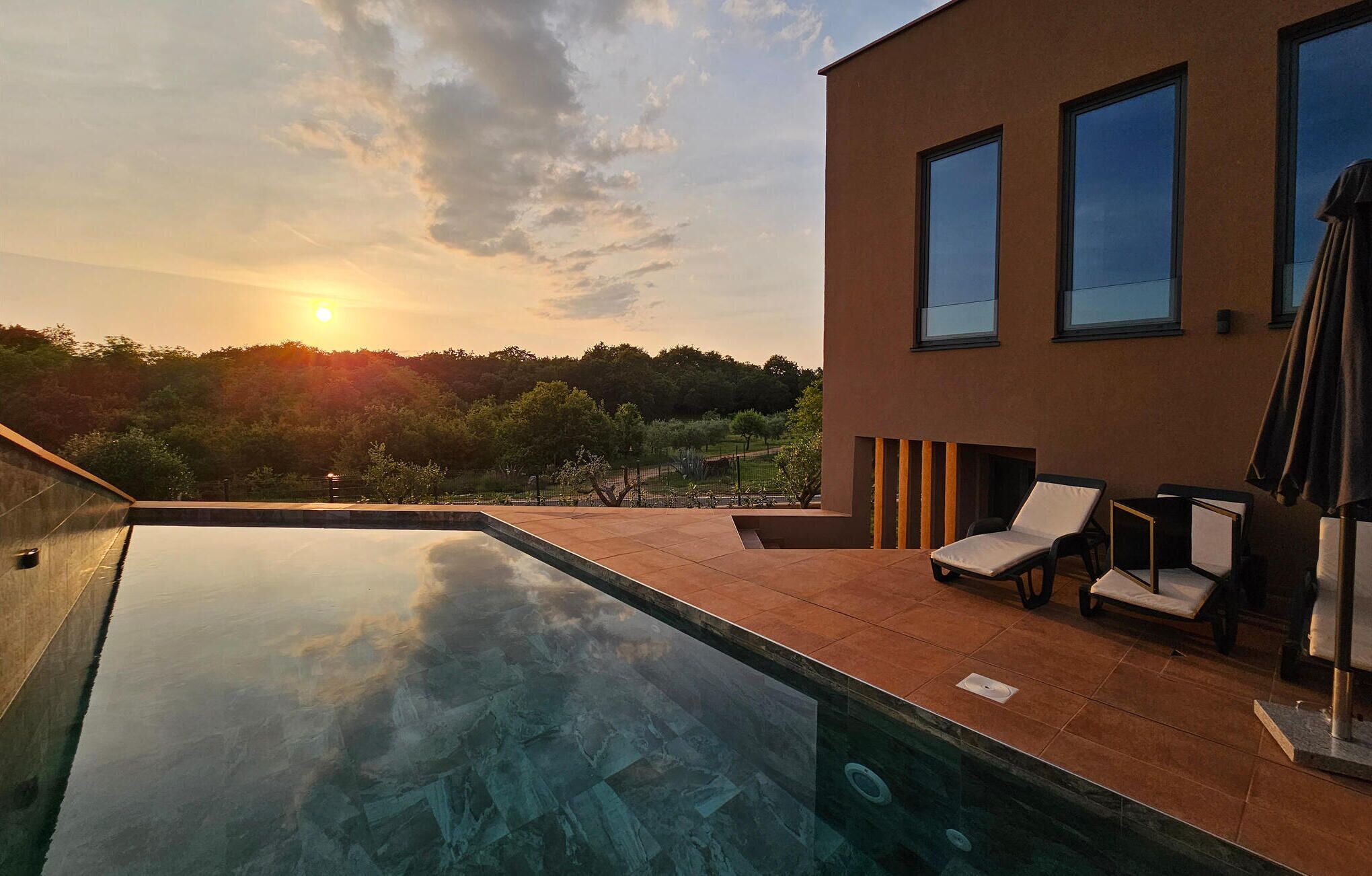 Un espace piscine extérieur moderne offrant une vue dégagée sur le coucher du soleil et la végétation environnante.