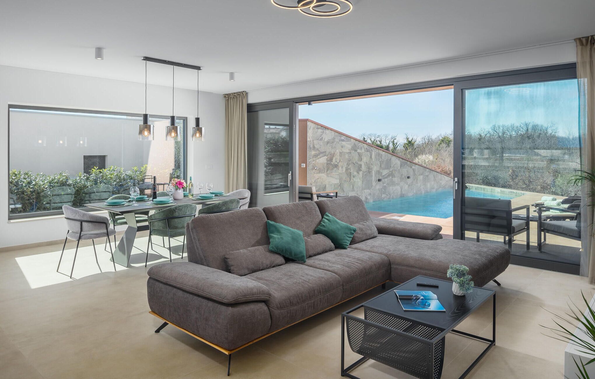 Una sala de estar moderna con un amplio sofá seccional gris, un comedor con mesa de vidrio y vistas a una piscina.