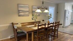 Uma sala de jantar com uma mesa de madeira, quatro cadeiras, um banco e duas luminárias fixadas na parede.