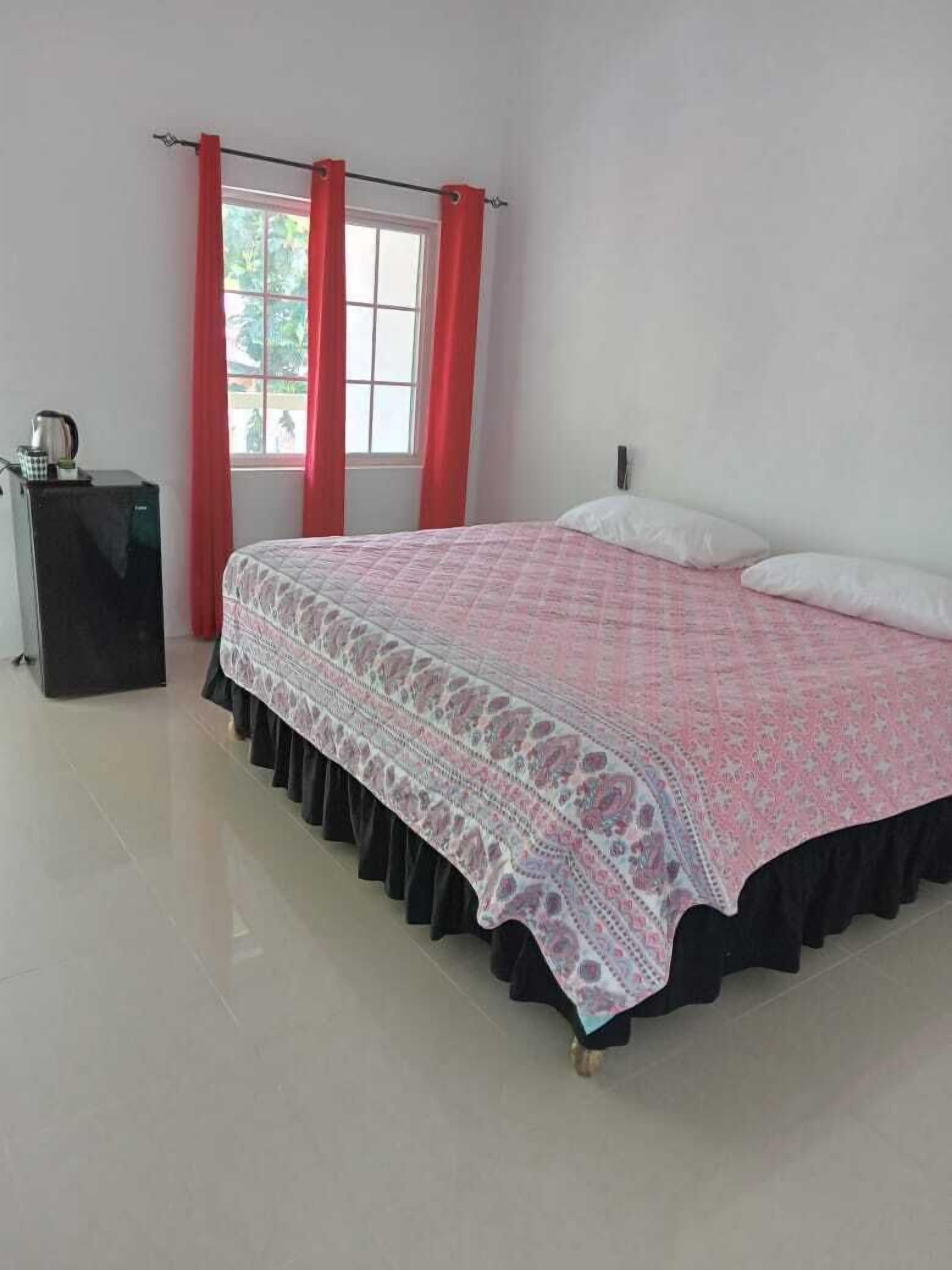 A bedroom with a bed, a nightstand, a window with red curtains, and a view outside.