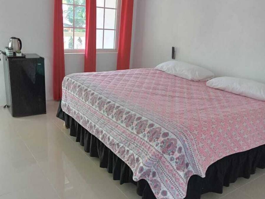 A bedroom with a bed, a nightstand, a window with red curtains, and a view outside.