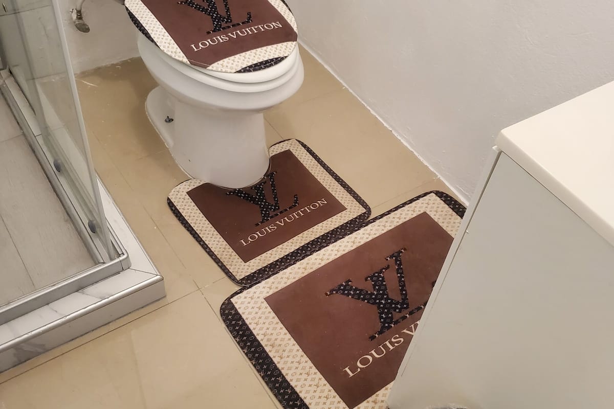 A bathroom with a toilet, a bidet, and two floor mats with the Louis Vuitton logo.