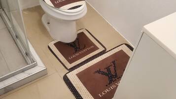 A bathroom with a toilet, a bidet, and two floor mats with the Louis Vuitton logo.