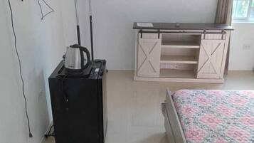 A bedroom with a bed, a desk, a kettle, and a TV mounted on the wall.