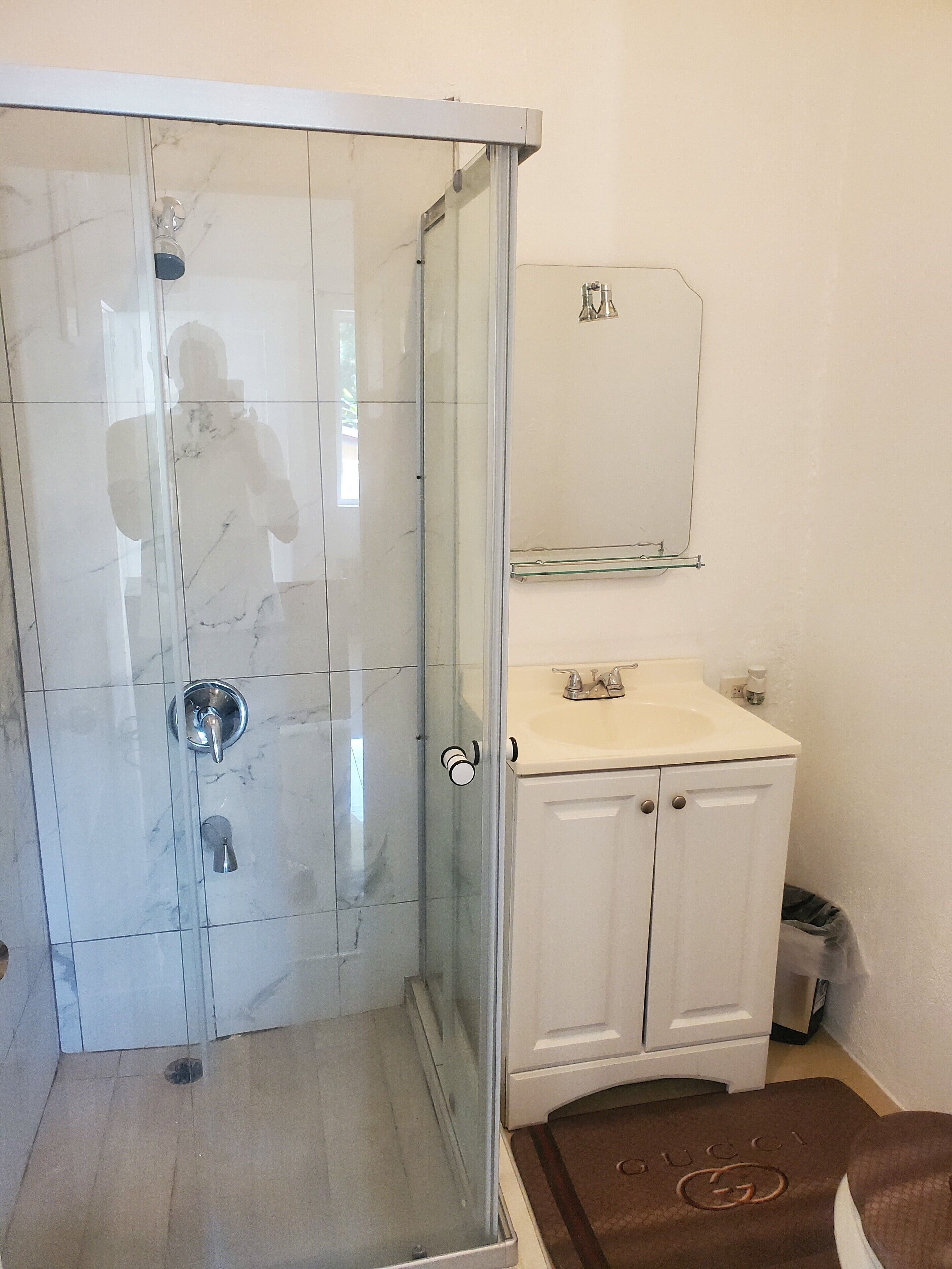 Un baño con ducha de vidrio, un lavamanos blanco con espejo arriba y un mueble debajo.