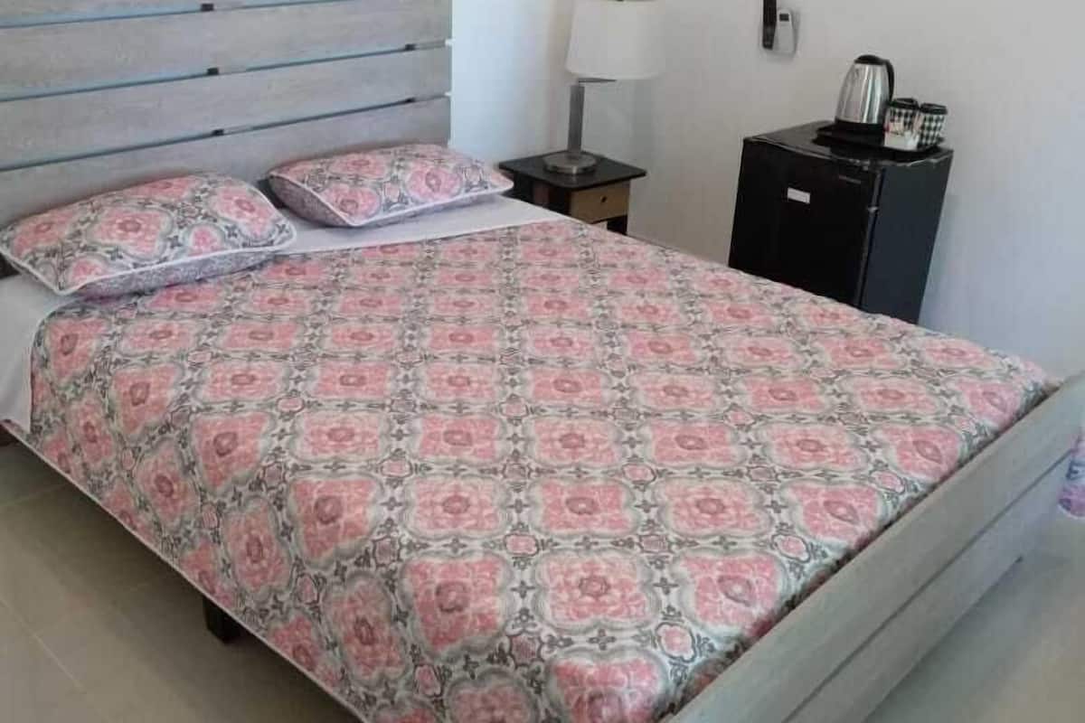 A bedroom with a bed, a nightstand, a lamp, and a small cabinet.