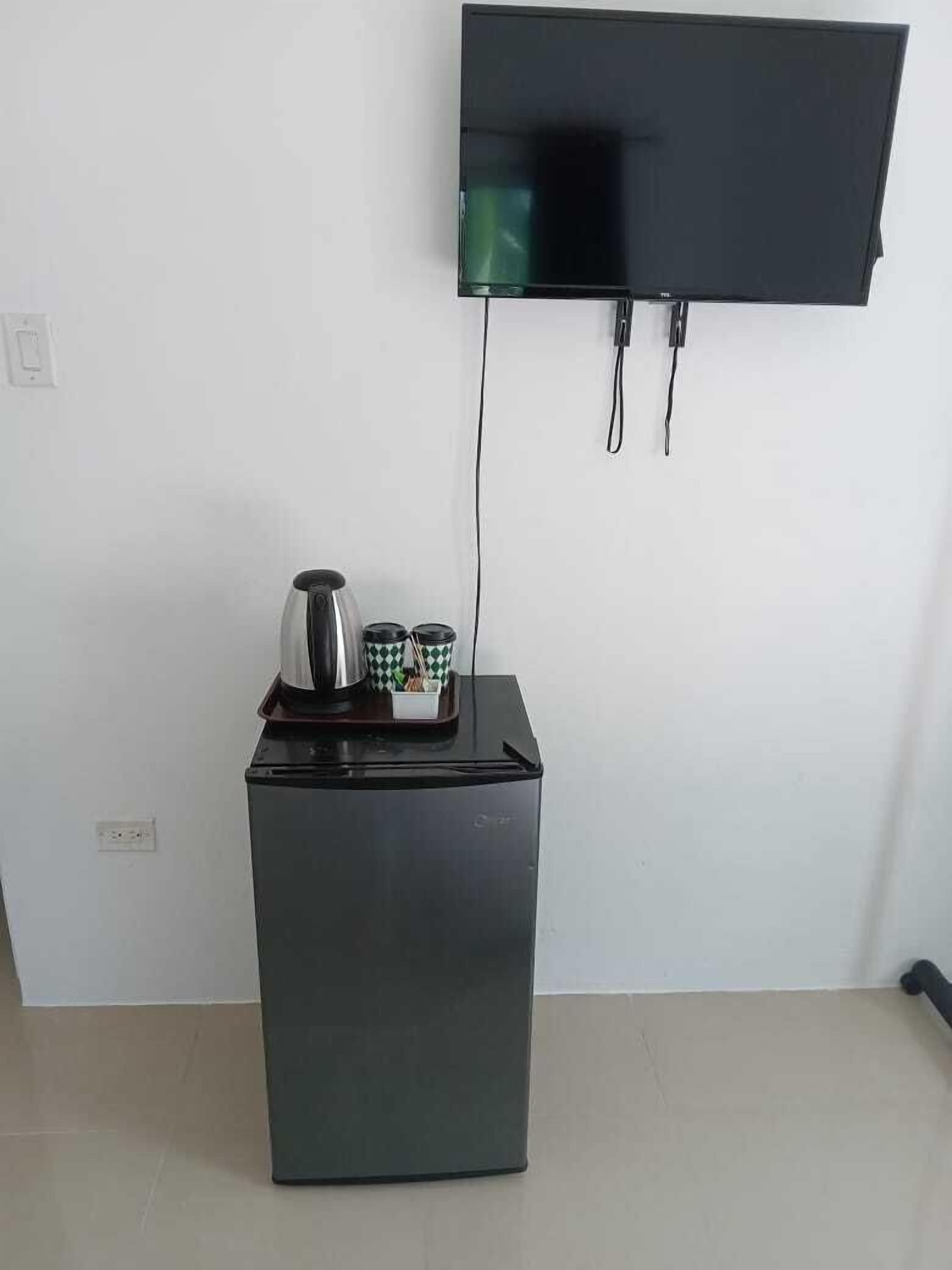 Un refrigerador pequeño negro con un televisor de pantalla plana montado en la pared superior.