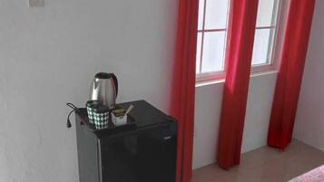 Een compacte kamer met een kleine, zwarte koelkast, een waterkoker en een bed met beddengoed met een patroon.