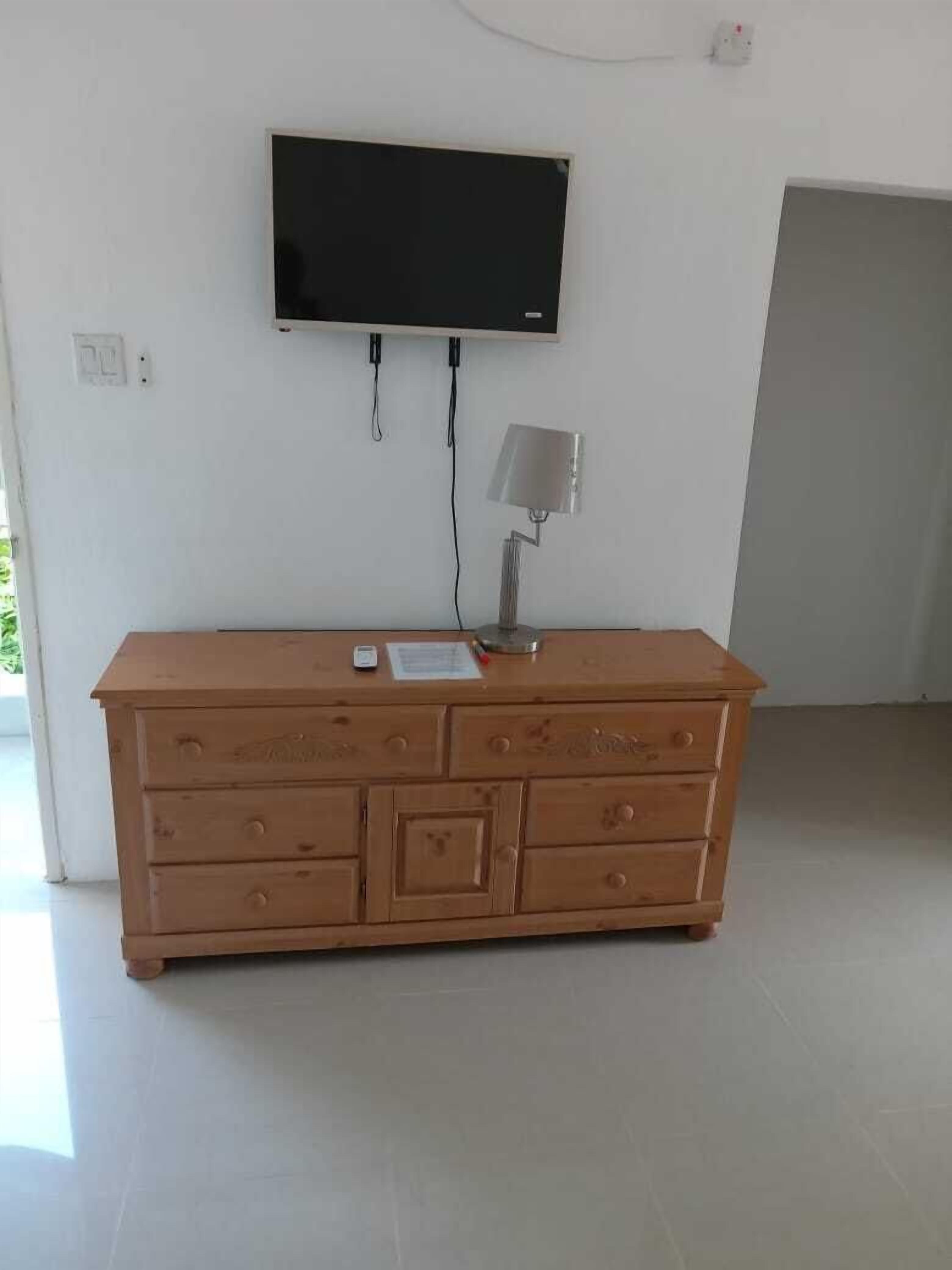 Uma cômoda de madeira com gavetas e uma TV de tela plana presa na parede acima.