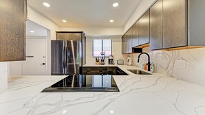 Une cuisine moderne dotée d’un îlot central, d’appareils électroménagers en acier inoxydable et d’un plan de travail en marbre.