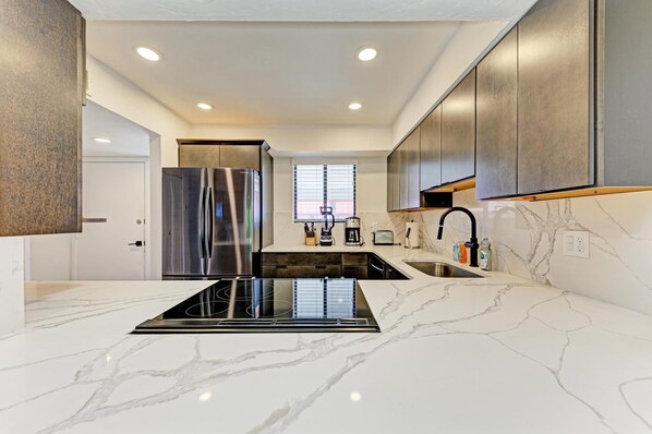 A modern kitchen with a central island, stainless steel appliances, and a marble countertop.