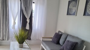 Ein modernes Wohnzimmer mit einem grauen Sofa, einem weißen Sessel und einem Glastisch mit Pflanze.