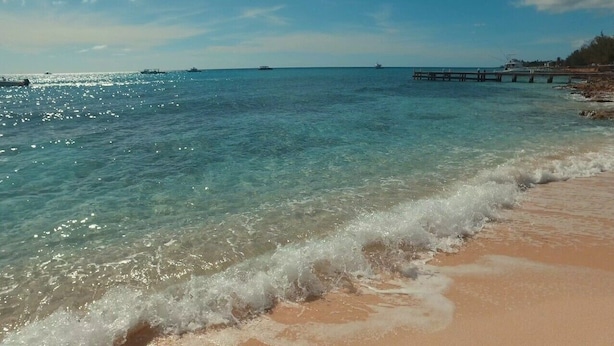 Ein Strand mit klarem Wasser, sandigem Ufer und einer Mole, die ins Meer führt.