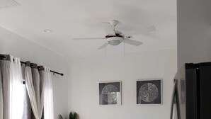Ein modernes Wohnzimmer mit einem weißen Sofa, einem Couchtisch mit Dekoration, einem Deckenventilator und zwei Wandbildern.