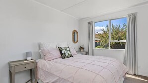 Un dormitorio con una cama grande, una mesita de noche, una ventana con cortinas y vistas a árboles y edificios.