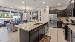 A modern kitchen with dark cabinetry, stainless steel appliances, and a large island with a sink. - Luxury 5BR Townhome: Private Pool & Resort Fun - 117 JW (Davenport)