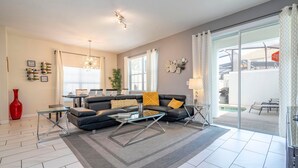 A modern living room with a sectional sofa, glass coffee table, and a large sliding glass door leading to a patio.