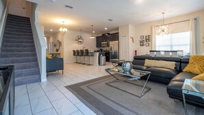 A modern living room with a staircase, a dining area, and a kitchen.