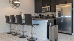 A modern kitchen with dark cabinets, stainless steel appliances, a central island with bar stools, and a decorative wall clock.