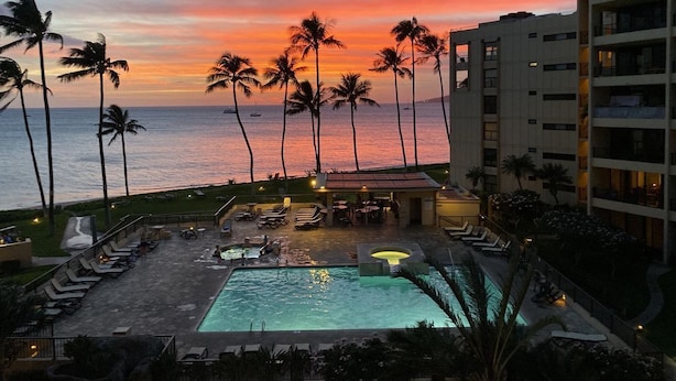 A hotel pool area with a sunset view, palm trees, and a building in the background. - SUGAR BEACH BLISS #2- BRAND NEW Designer Luxury-Ocean/Volcano Views 5 STAR Owner (Kihei)
