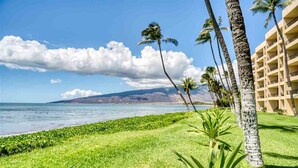 A beachfront hotel with a grassy lawn, palm trees, and a view of the ocean and mountains. - SUGAR BEACH BLISS #2- BRAND NEW Designer Luxury-Ocean/Volcano Views 5 STAR Owner (Kihei)