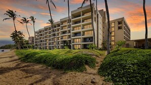 A multi-story hotel with balconies, located near a beach with palm trees and a sunset view. - SUGAR BEACH BLISS #2- BRAND NEW Designer Luxury-Ocean/Volcano Views 5 STAR Owner (Kihei)