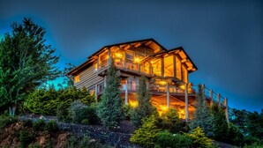 Una cabaña de troncos de varios niveles con balcones, rodeada de un bosque denso.