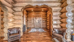 Ein rustikales Holzhaus-Interieur mit Holzboden, zwei Ledersesseln und einer zentralen Tür mit geschnitzten Verzierungen.