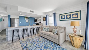 A modern kitchen with a central island, a living area with a sofa and bar stools, and a decorative lamp. - Beach Service Included! 100 Yards To Private Beach! Gulfview I 112 (Destin)