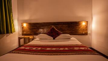 A neatly made bed with a patterned bedspread, a wooden headboard with wall-mounted lights, and a small bedside table.