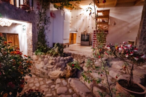 A stone courtyard with potted plants and flowers, a rustic interior with wooden beams, and a stone wall. - MAMA GREEN Eco Lodge l Permaculture Farm l Farm To Table (Urubamba)