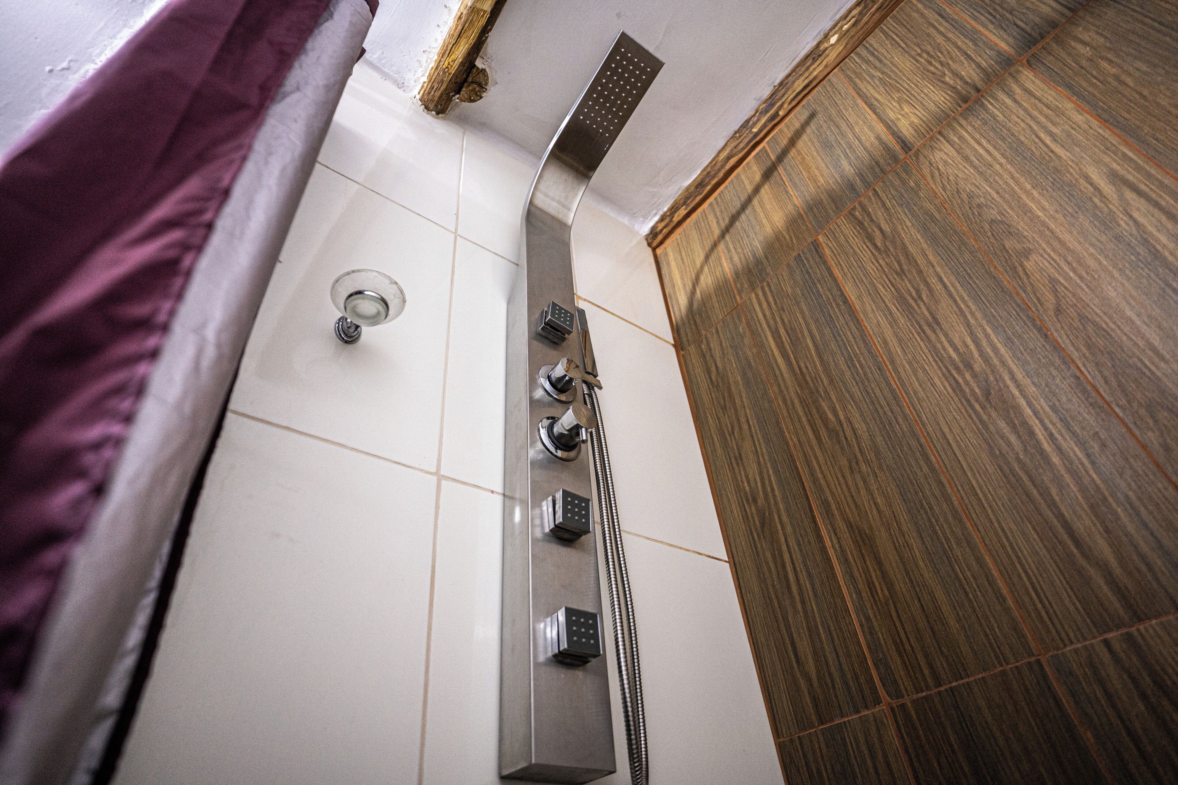 A modern bathroom with a shower, a control panel, and a wooden wall.