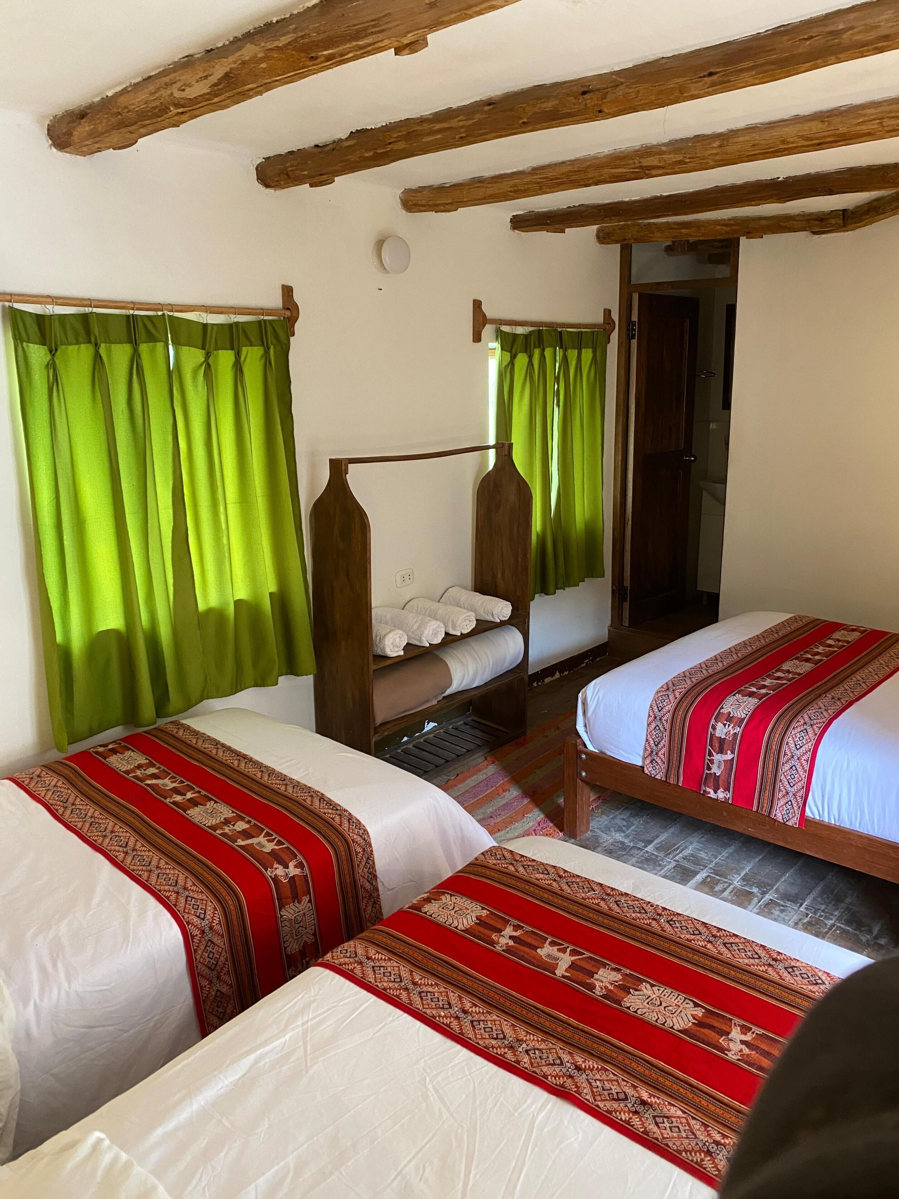 A room with two beds, a wooden ceiling, and a green curtain.