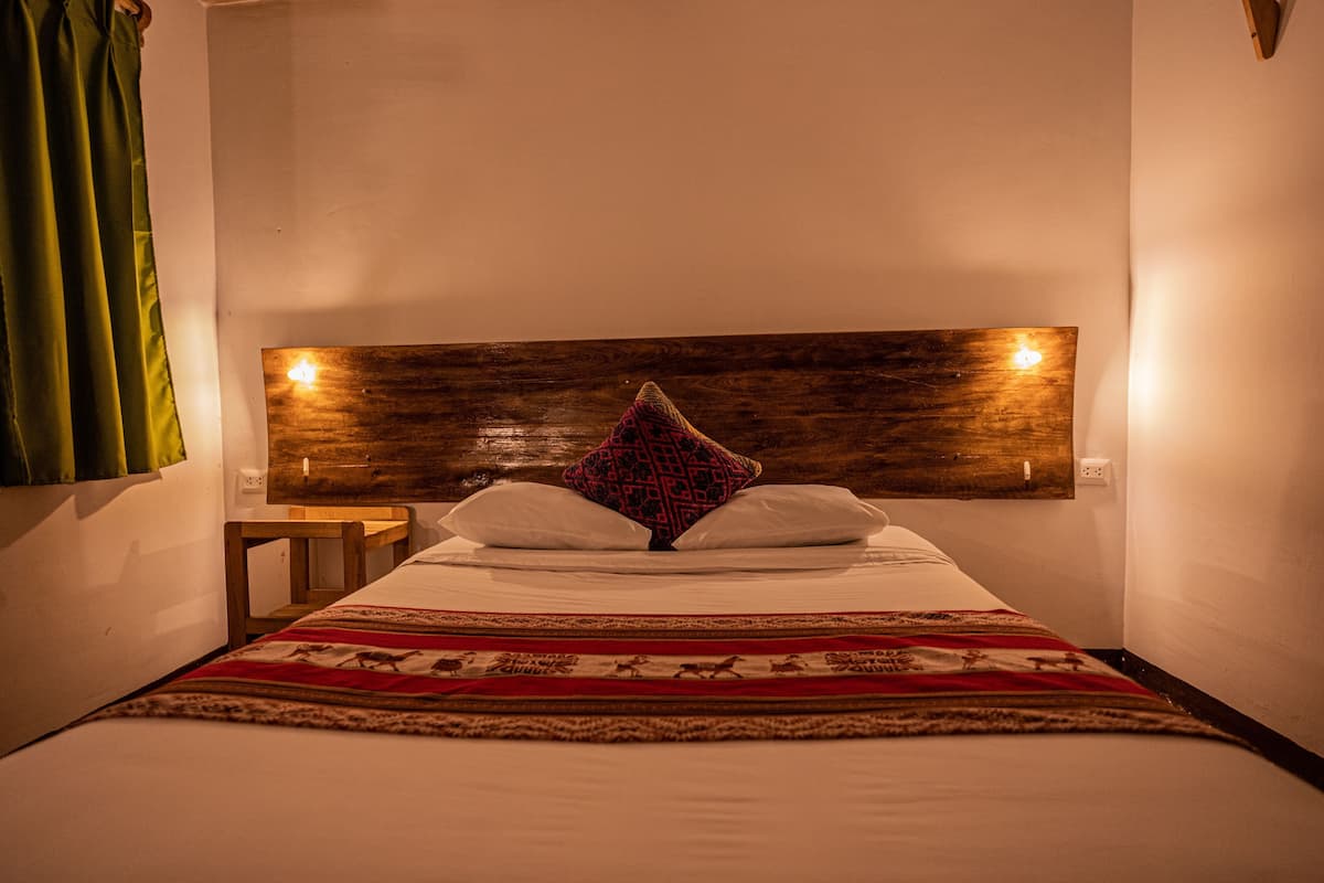 Ein ordentlich bezogenes Bett mit einem gemusterten Überwurf, ein Holz-Kopfteil mit an der Wand befestigten Lampen und ein kleiner Nachttisch.