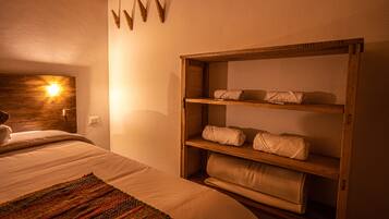 Une chambre d’hôtel avec un lit, une étagère en bois où sont posées des serviettes et un luminaire fixé au mur.