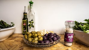 A wooden table with a glass bowl containing olives, a bottle of olive oil, and a jar of salt. - MAMA GREEN Eco Lodge l Permaculture Farm l Farm To Table (Urubamba)