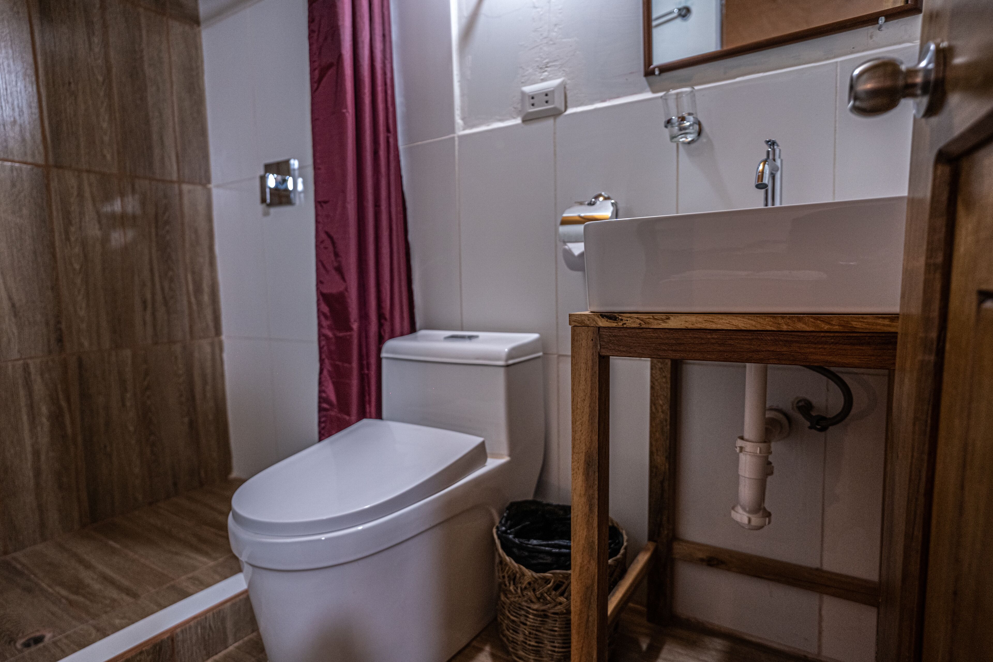 A bathroom with a toilet, shower, sink, and wooden cabinet.