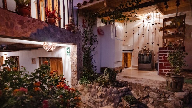 A stone courtyard with a rustic stone wall, potted plants, and a small garden area with flowers. - MAMA GREEN Eco Lodge l Permaculture Farm l Farm To Table (Urubamba)