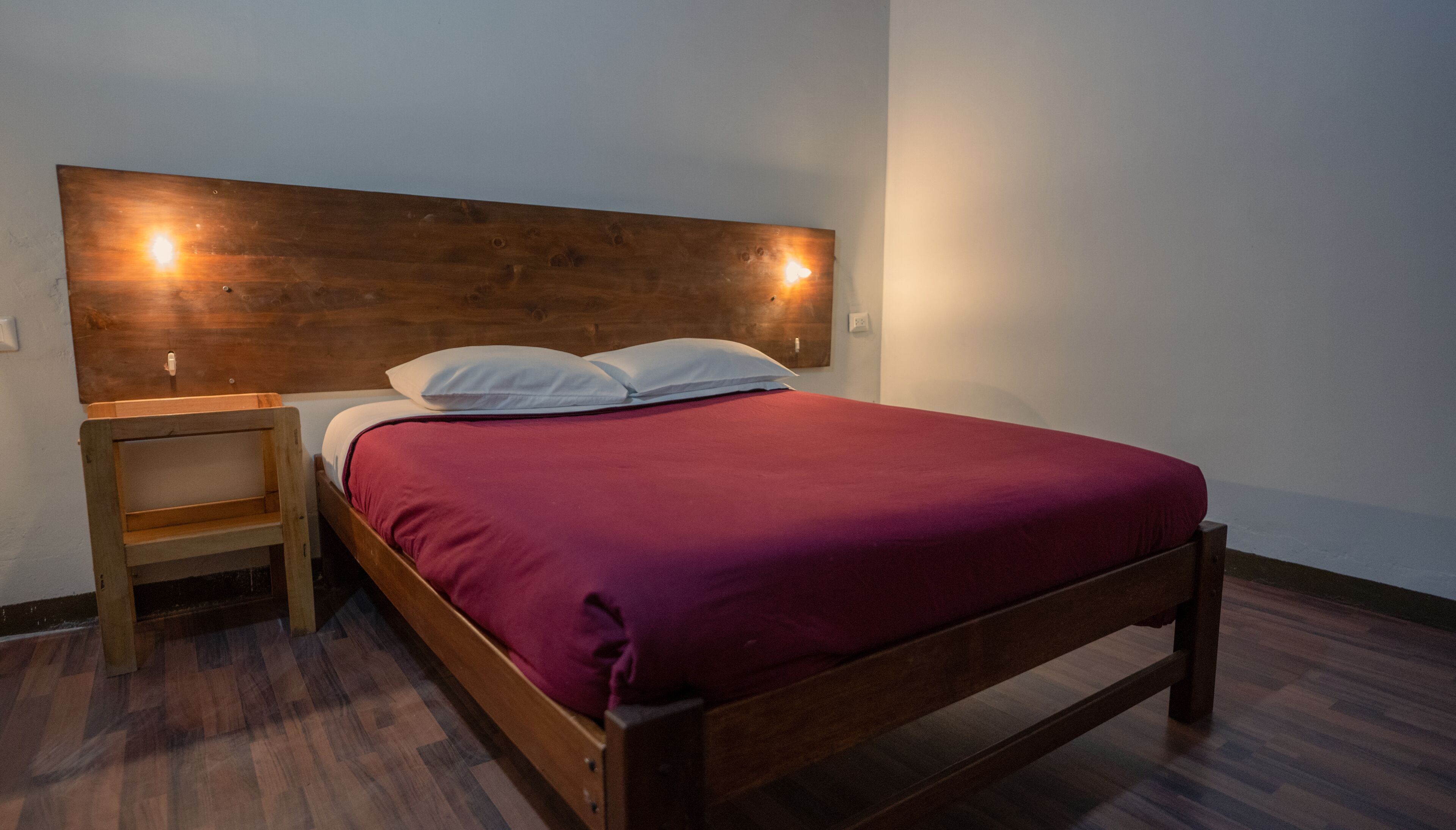 A single bed with a wooden headboard, a nightstand, and a red bedspread.
