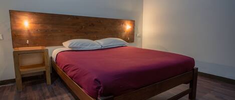 A single bed with a wooden headboard, a nightstand, and a red bedspread.
