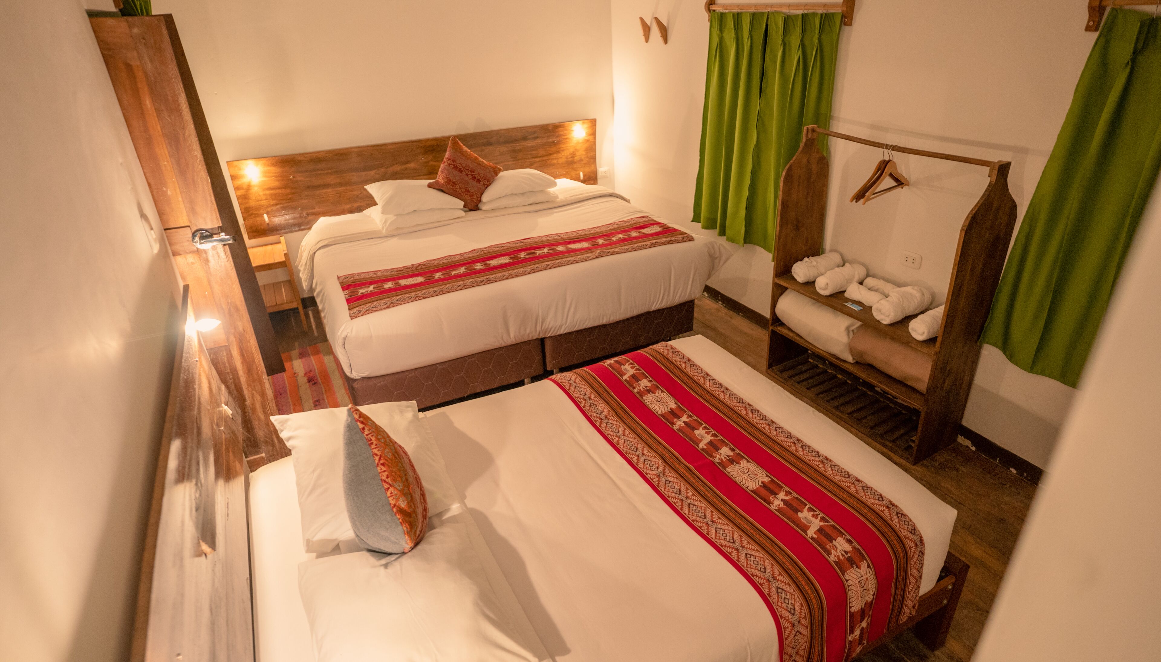 Habitación de hotel con dos camas, cabecero de madera, cortina verde y repisa con toallas.