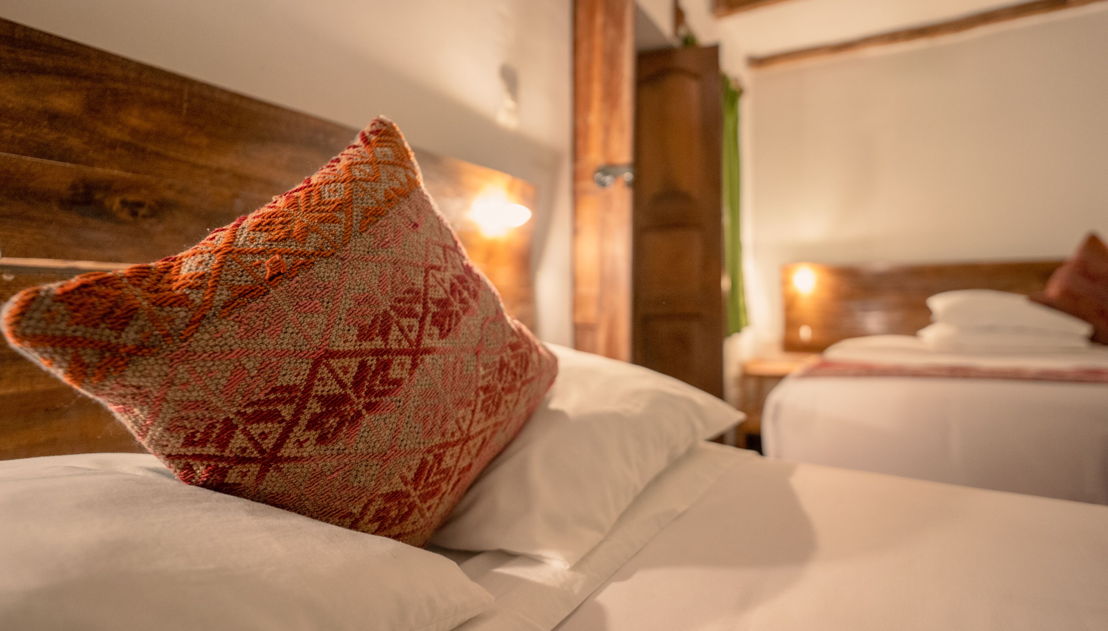 Una habitación de hotel con cabecera de madera, almohada decorativa estampada y cama bien hecha con sábanas blancas.